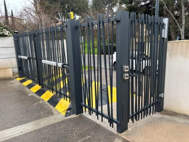 Portail à barreaudage noir motorisé ouvert avec portillon piéton, marquage au sol jaune et noir