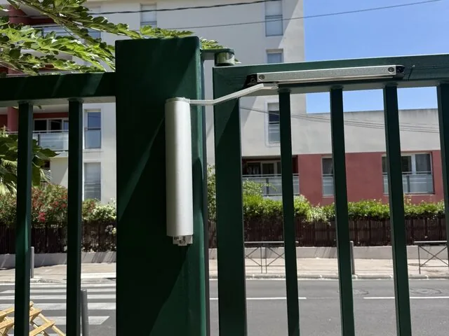 Gros plan sur le vérin et le bras de motorisation d’un portail vert
