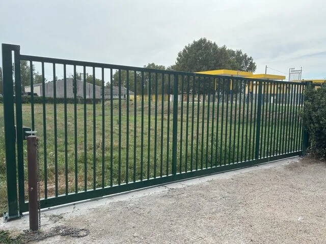 Portail coulissant noir sur rail, ouvert sur terrain engazonné